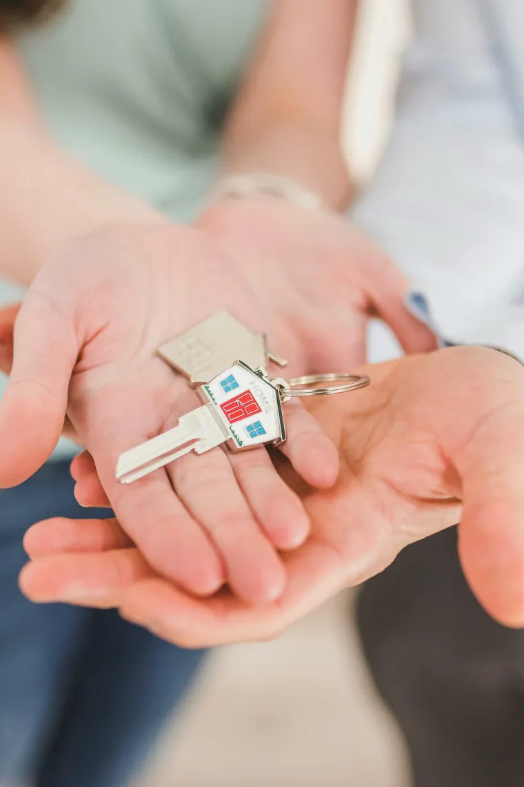 Hand receiving a key with a house-shaped keychain